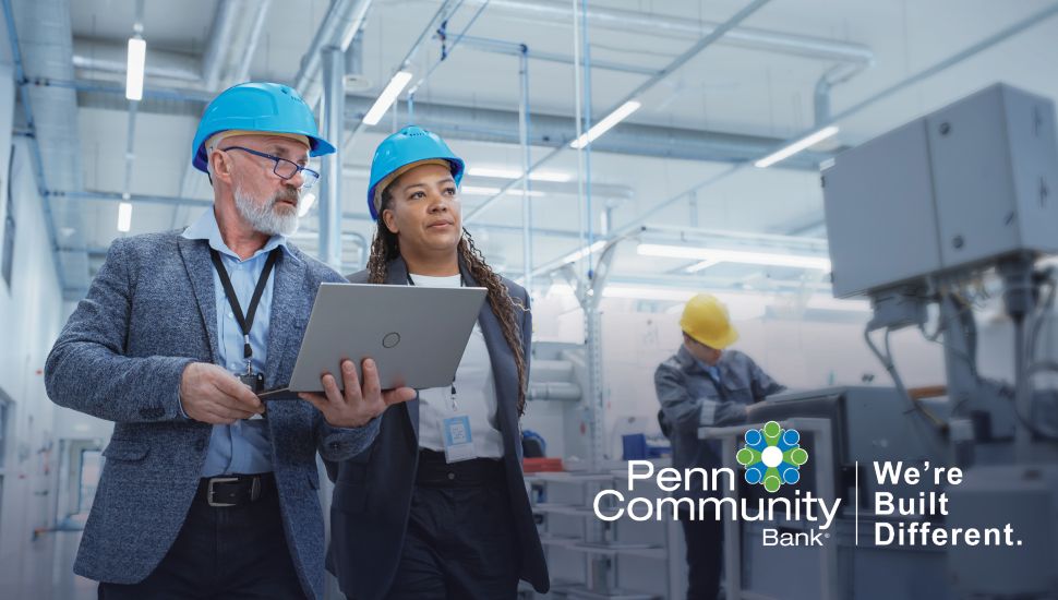Penn Community Bank advisors review digital payment operations with a business owner inside a modern manufacturing facility.