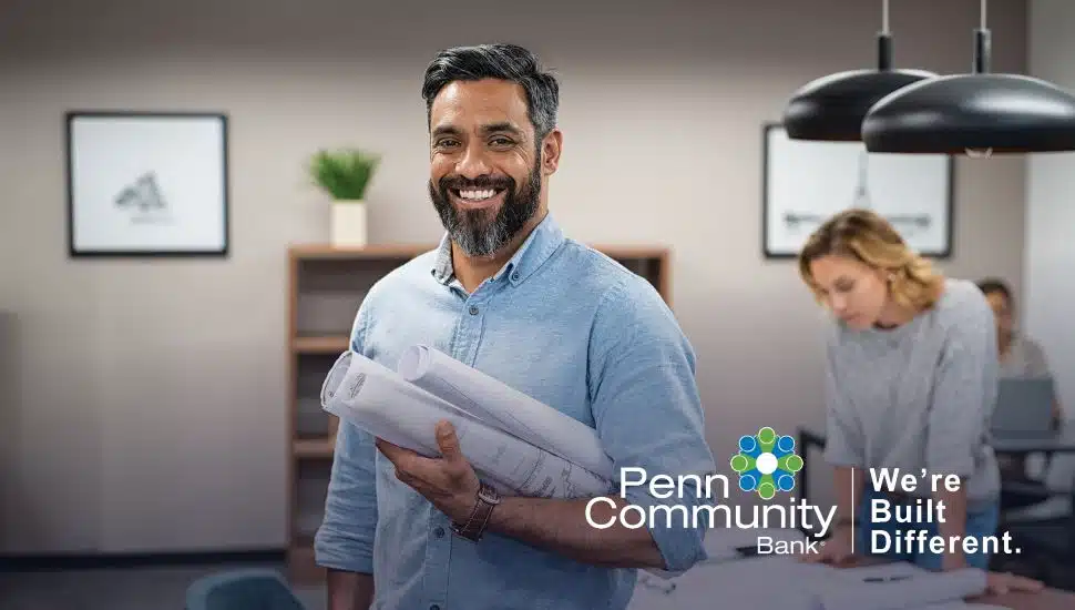Small business owner holding blueprints in a collaborative workspace supported by Penn Community Bank.