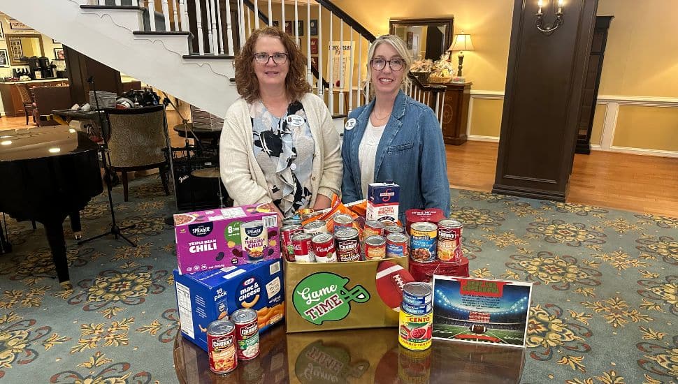 Two women stand behind some of the food items collected for the Freedom Village at Brandywine “Soup for the Super Bowl” food drive