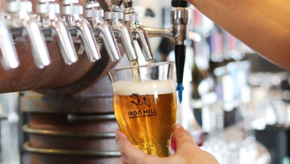 A hand pours a beer from a tap into an Iron Hill-branded glass.
