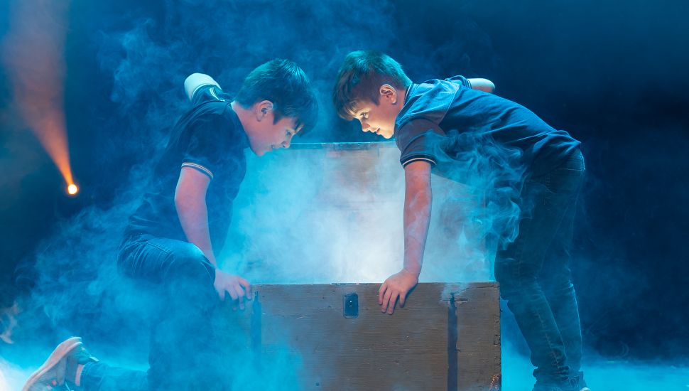 Two young boys open a mysterious treasure chest in a smoke-filled magic shop scene from the immersive Enchanted production in Lancaster, PA.