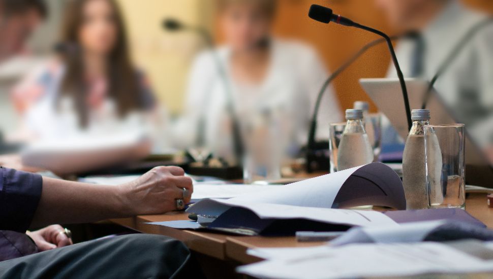 Microphones at table with people sitting and discussing township meeting.
