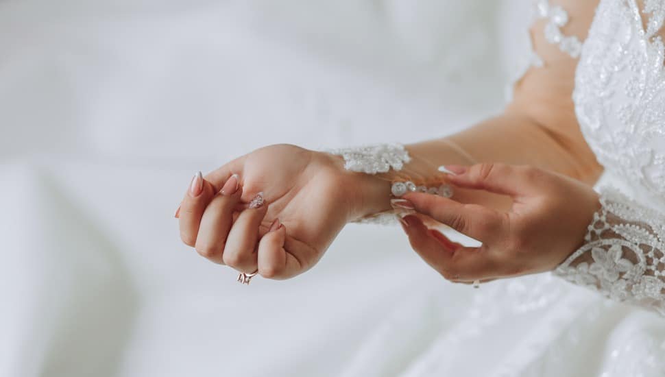 The bride fastens the lace sleeves.