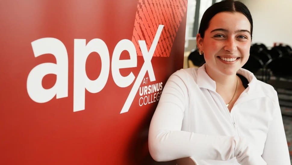 An Ursinus student smiles next to an APEX sign.
