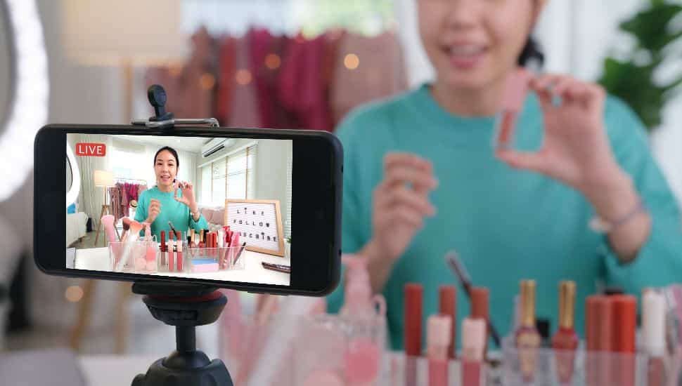 Woman films on phone for livestream shopping as she shows makeup.