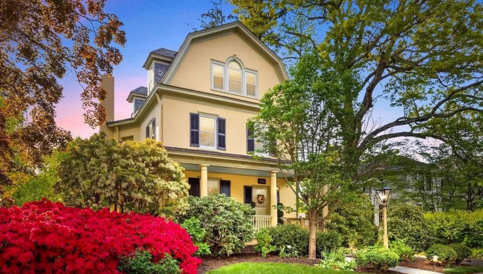 Yellow home with black shutters surrounded by trees and bushes.