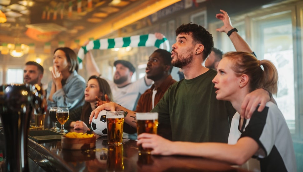 Group of enthusiastic soccer fans intently watching a live game on tv in a pub, reacting with excitement, drinking beer, and eating chips.