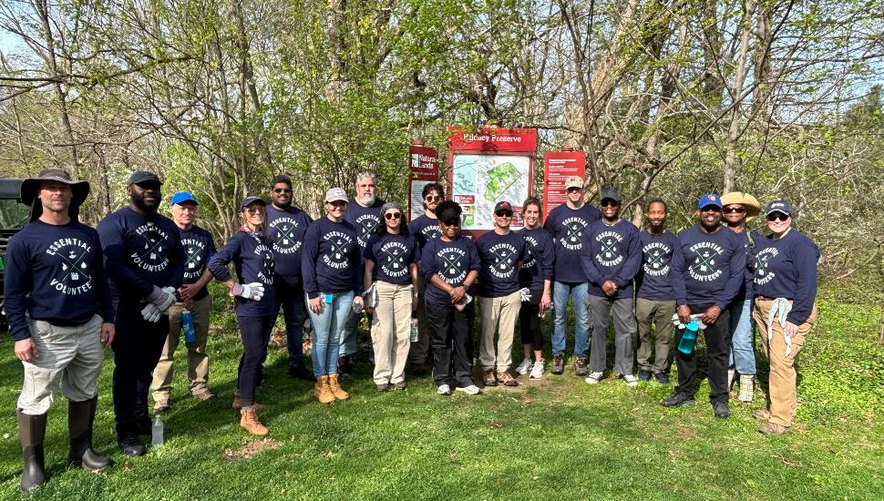 A group of volunteers wearing matching shirts stands outdoors at Hildacy Preserve, posing together after participating in a tree planting and conservation project.