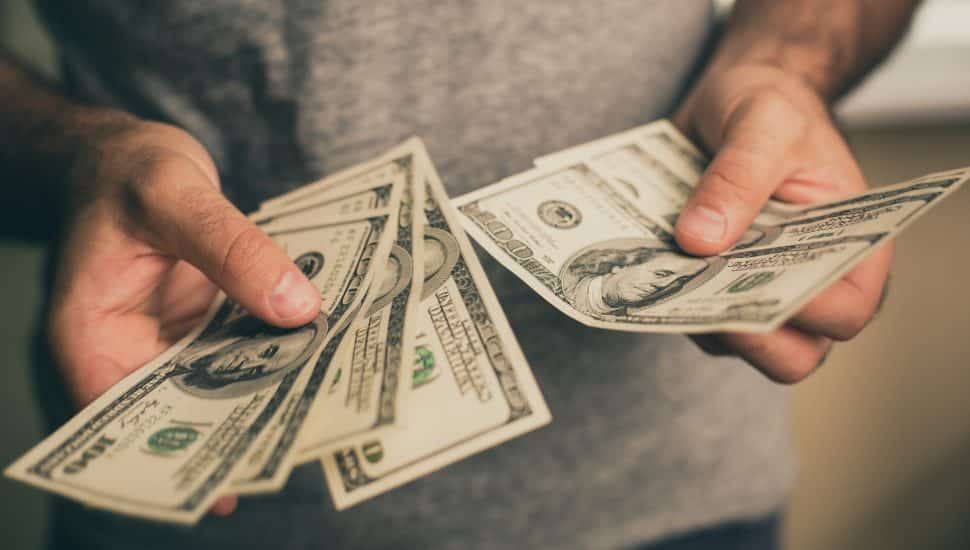 Man in gray shirt holds spread of money in hands.