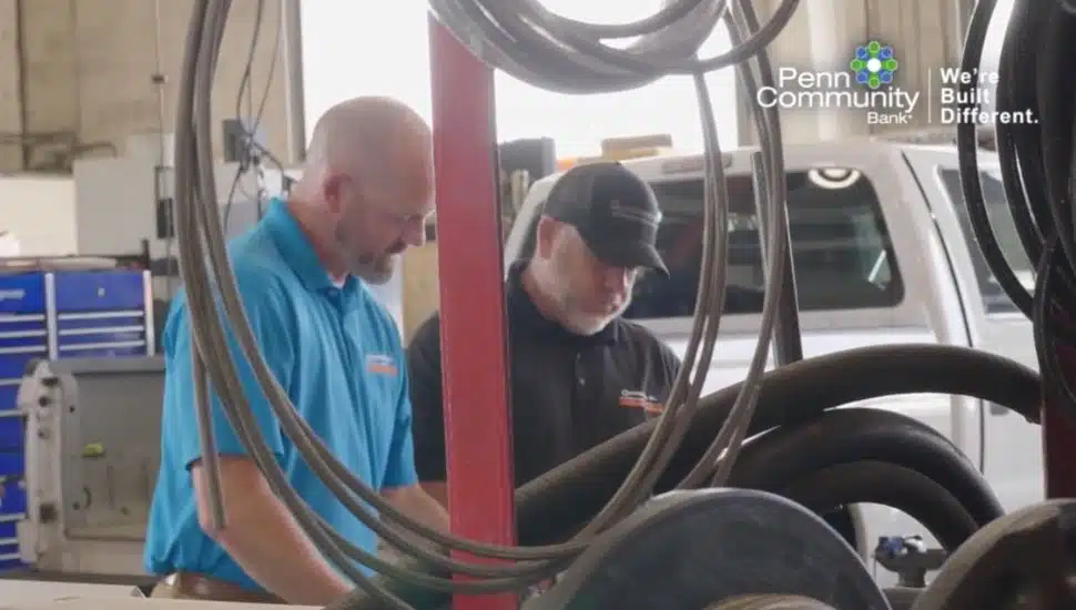 Two Guidemark employees reviewing equipment inside a maintenance facility, with Penn Community Bank branding visible in the background.