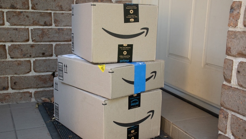 Three Amazon Prime boxes stacked on a residential doorstep next to a brick wall and white door.