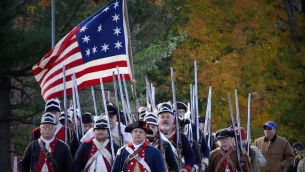 Revolutionary Was Reenactors march under a Colonial flag.