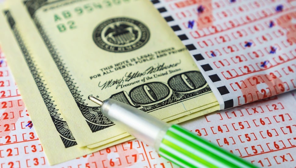 A lottery ticket alongside a pencil and a stack of $100 bills.
